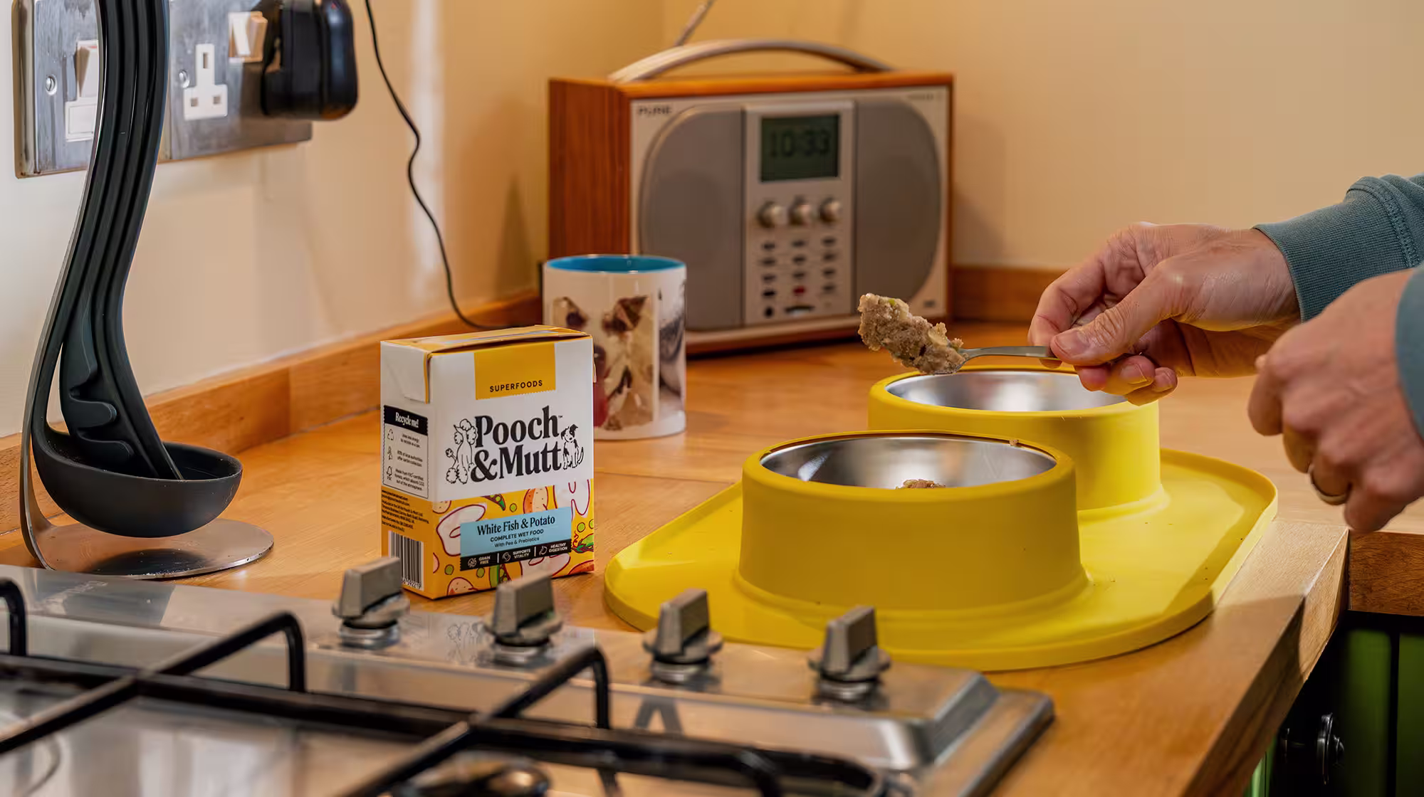 A dog owner spoons Pooch & Mutt Wet Food into a yellow dog bowl